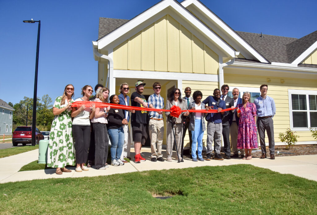 Habitat and HOPE NC staff, future residents, and elected officials pose with a big ribbon in front of a HOPE NC duplex at Weavers Grove.